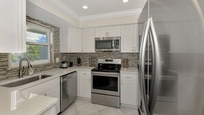 A modern kitchen with white cabinets, stainless steel appliances, a tiled backsplash, and a window providing natural light. - Blue Wave | Prime Siesta Key - Walk to Beach & Village, Plus Private Pool (Siesta Key)