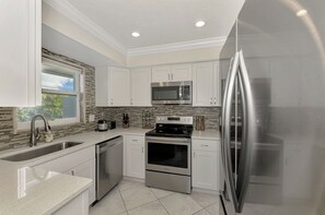 A modern kitchen with white cabinets, stainless steel appliances, a tiled backsplash, and a window providing natural light.
