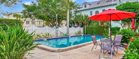 A swimming pool with a 4 FT depth, surrounded by a white fence, with chairs and a red umbrella.