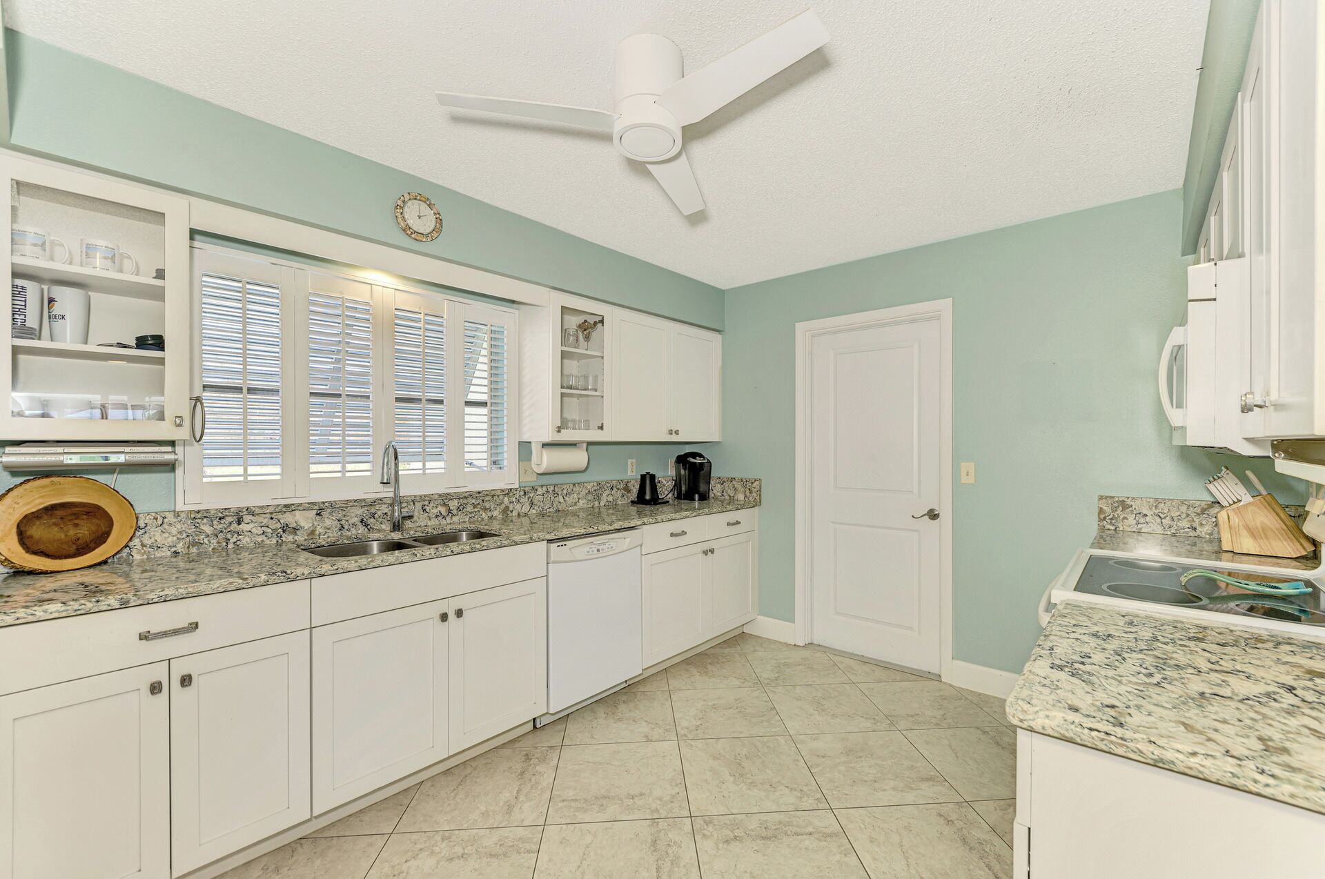 A kitchen with white cabinets, a granite countertop, a built-in oven, and a ceiling fan.
