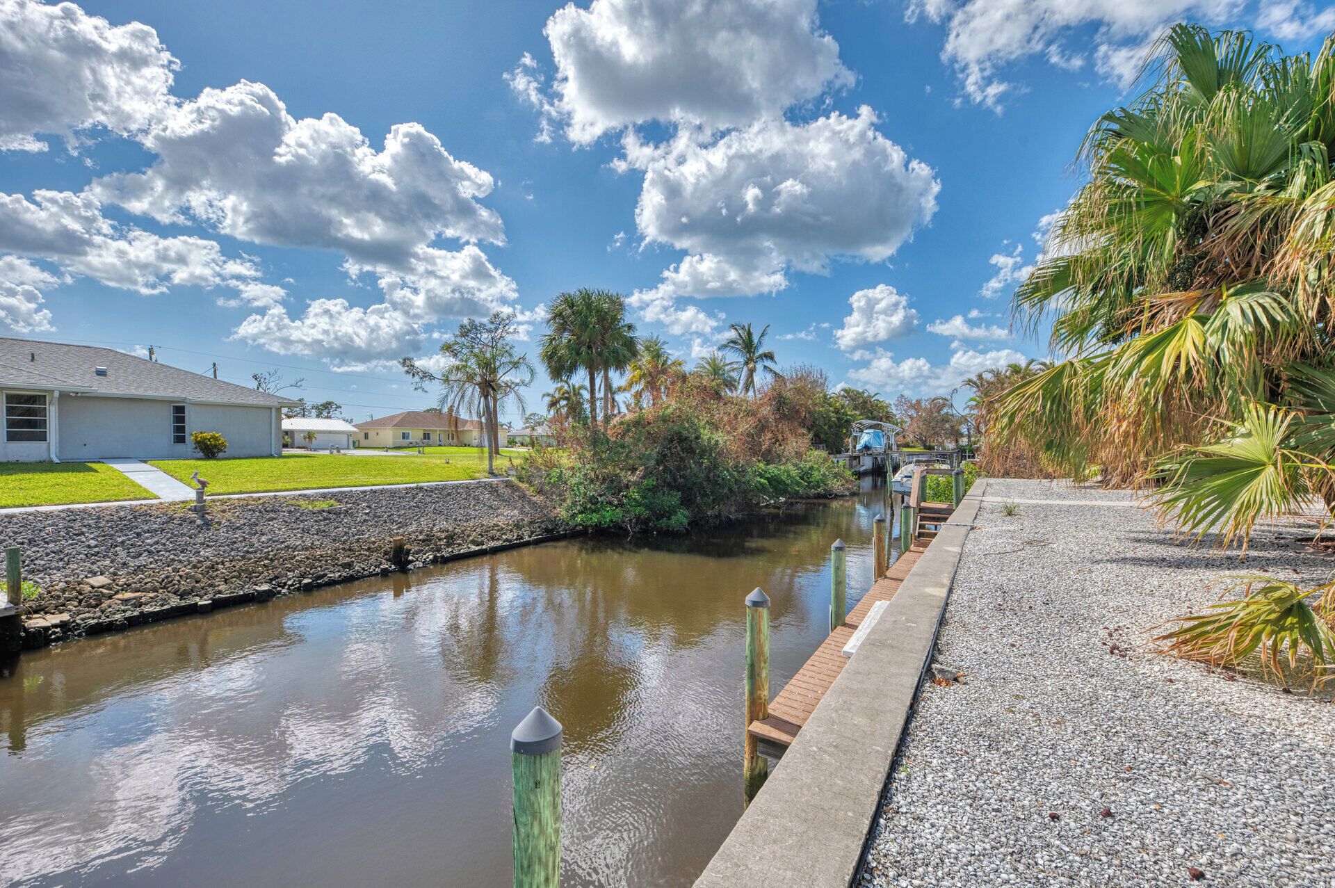 A canal with a wooden dock, a house, and palm trees.