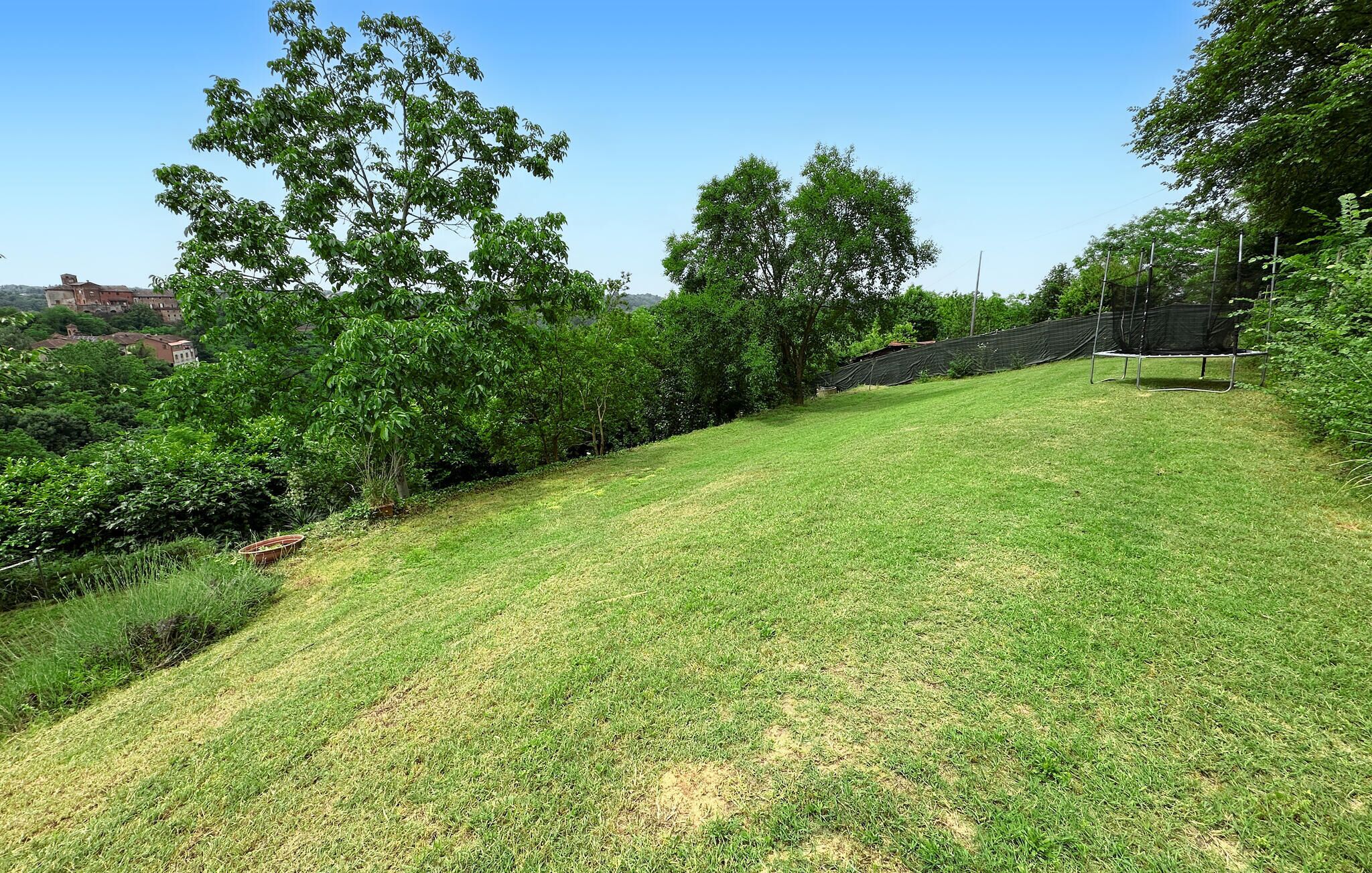 A grassy slope with trees and a building in the background.