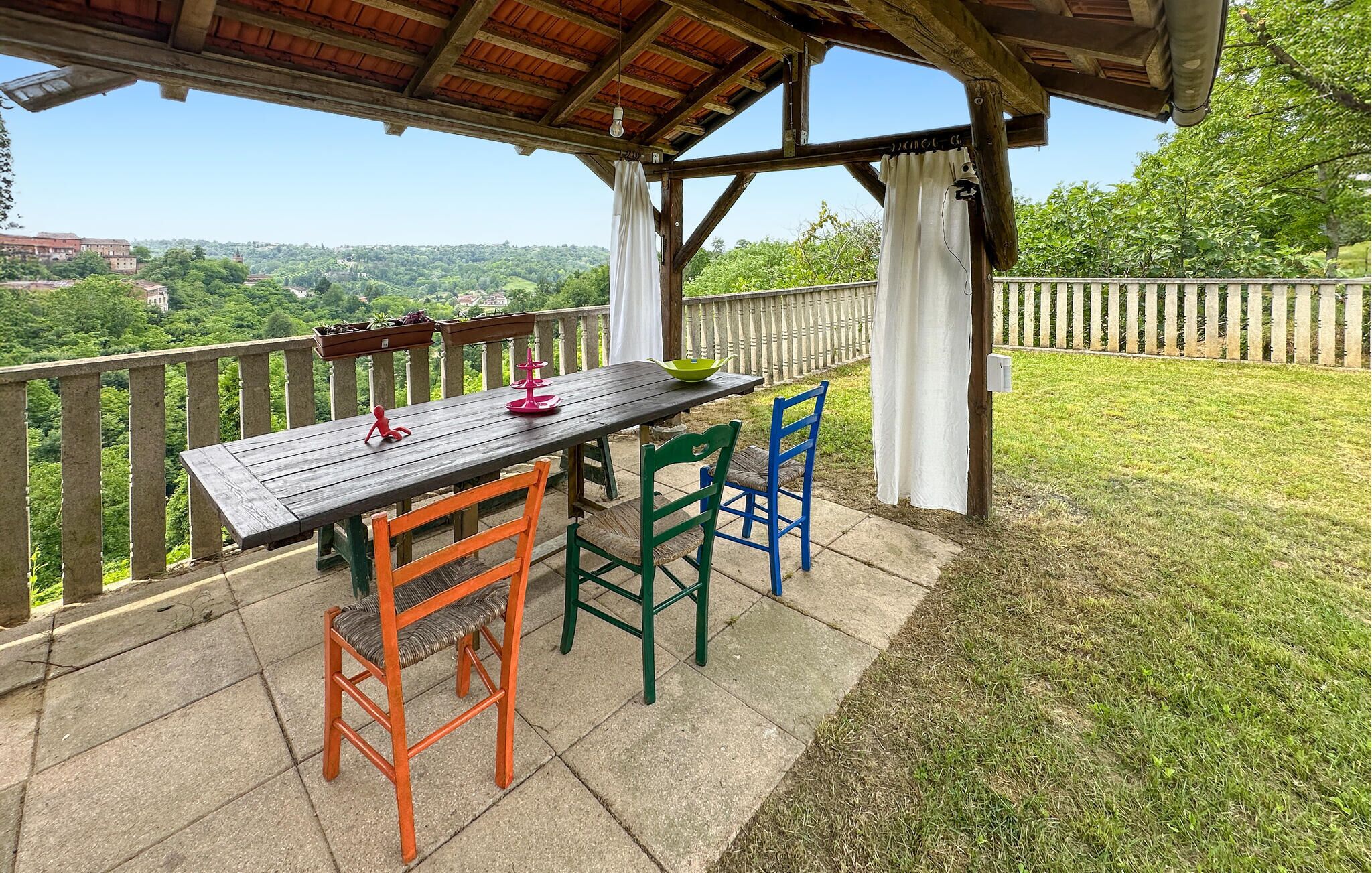 Une terrasse extérieure avec une table et des chaises en bois, une vue sur la campagne et une clôture en bois.