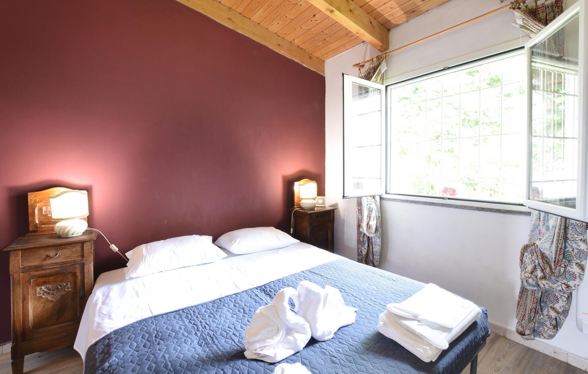 Une chambre à coucher avec un lit, deux tables de chevet, une fenêtre avec des rideaux et un plafond en bois.