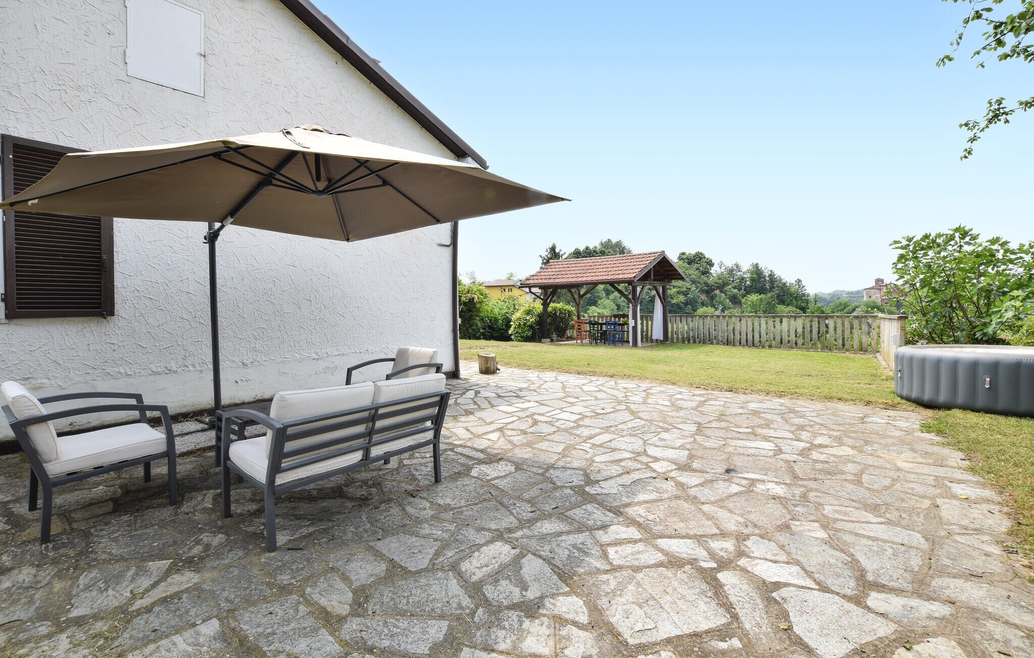 Un patio de piedra con mobiliario exterior y un gran paraguas.