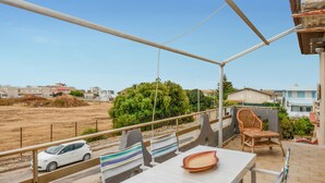A balcony with a table and chairs, a car parked in the background, and a view of a residential area with houses and greenery. - Amazing apartment in Santa Croce Camerina (Santa Croce Camerina)