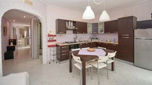 A modern kitchen with dark wooden cabinets, a stainless steel refrigerator, and a dining area with a wooden table and white chairs. - Amazing apartment in Santa Croce Camerina (Santa Croce Camerina)