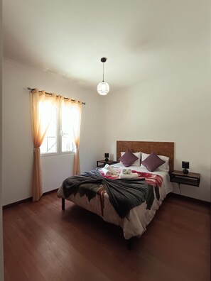 A bedroom with a bed, a nightstand, a lamp, and a window with curtains. - Dotty's House (Santa cruz)