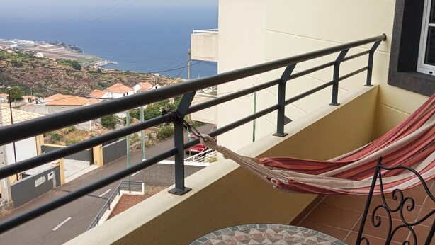 Un balcon avec vue sur la mer, un hamac et une table carrelée.