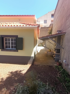 A building with a tiled roof, a window with shutters, and a staircase leading to a covered area with a table and chairs. - Dotty's House (Santa cruz)