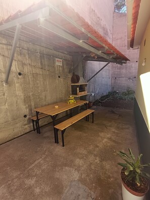 A concrete outdoor area with a wooden table and benches, a small garden with potted plants, and a metal structure overhead. - Dotty's House (Santa cruz)