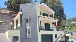 Une maison moderne à deux étages, avec une façade grise, une porte de garage verte et un balcon.