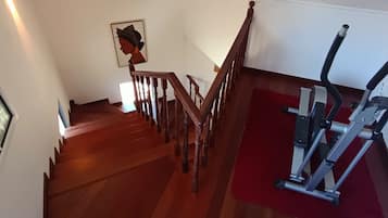 Een trap met houten leuningen die uitkomt op een plateau, waar een loopband op een rode mat staat.