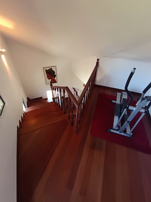 A staircase with wooden railings leading to a landing where a treadmill is placed on a red mat. - Dotty's House (Santa cruz)