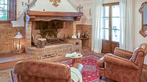 Ein gemütliches Wohnzimmer mit Kamin aus Naturstein, Ledersesseln und einem roten Teppich mit Muster.