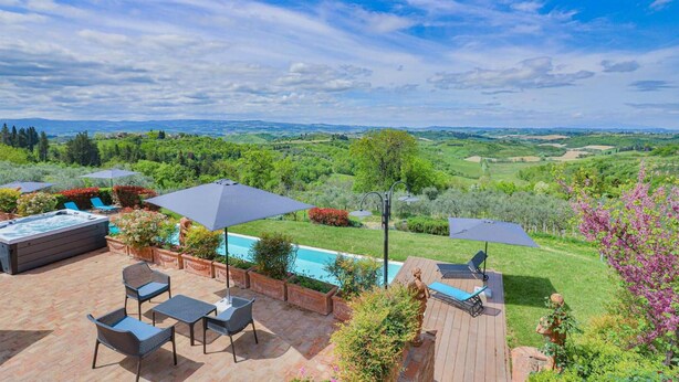 Eine Terrasse mit Gartenmöbeln, einem Whirlpool und Sonnenschirmen mit Blick auf eine üppige Landschaft.