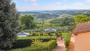 Ein Garten mit einem Pfad, der zu einem Gebäude führt, umgeben von üppiger Vegetation und einem malerischen Ausblick auf sanfte Hügel.