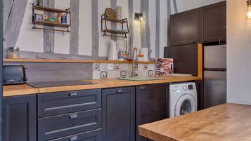 A modern kitchen with dark cabinets, a wooden countertop, a Breville toaster, a Samsung washing machine, and a wooden dining table.