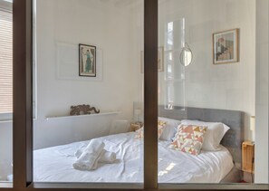 A bedroom with a bed, a bedside table, a mirror, and a picture on the wall.