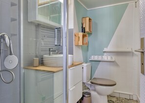 A modern bathroom with a glass-enclosed shower, a sink with a wooden countertop, a toilet, and a small wooden cabinet above the toilet.