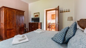 Ein Schlafzimmer mit einem Bett, einem Holzschrank, einem Fernseher und einem Essbereich, der durch eine offene Tür sichtbar ist.