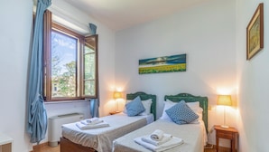 A room with two beds, each with a pillow and a rolled towel. There is a window with curtains, a painting on the wall, and a lamp on each bedside table. - Lovely apartment in Montone with WiFi (Montone)