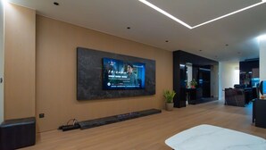 Un vestíbulo moderno con una televisión de pantalla plana grande montada en una pared oscura, piso de madera y una zona de recepción.