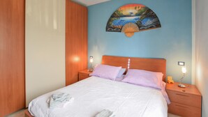 A bedroom with a bed, two bedside tables, a nightstand, a wooden wardrobe, and a wall painting.