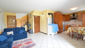 A living room with a blue sofa, a patterned rug, and a kitchen area with wooden cabinets and a tiled floor.