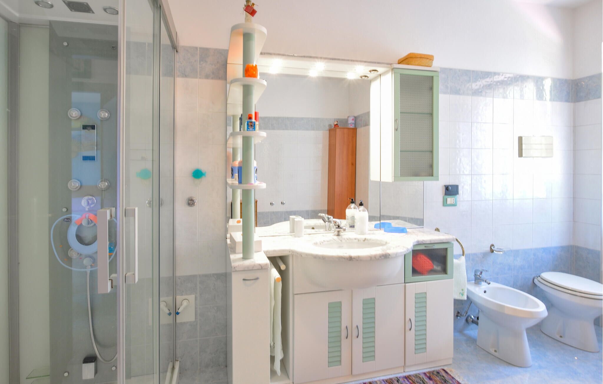 Un baño con cabina de ducha de vidrio, un lavabo con espejo, un inodoro y un mueble con contraventanas verdes.
