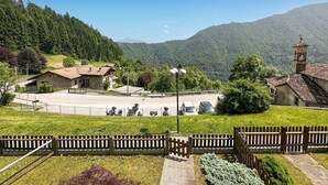 A rural setting with a stone building, a church with a bell tower, and a fenced area with parked motorcycles.
