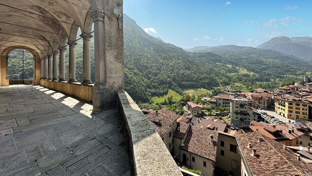 A stone structure with columns and an arched entrance overlooking a valley with traditional buildings.