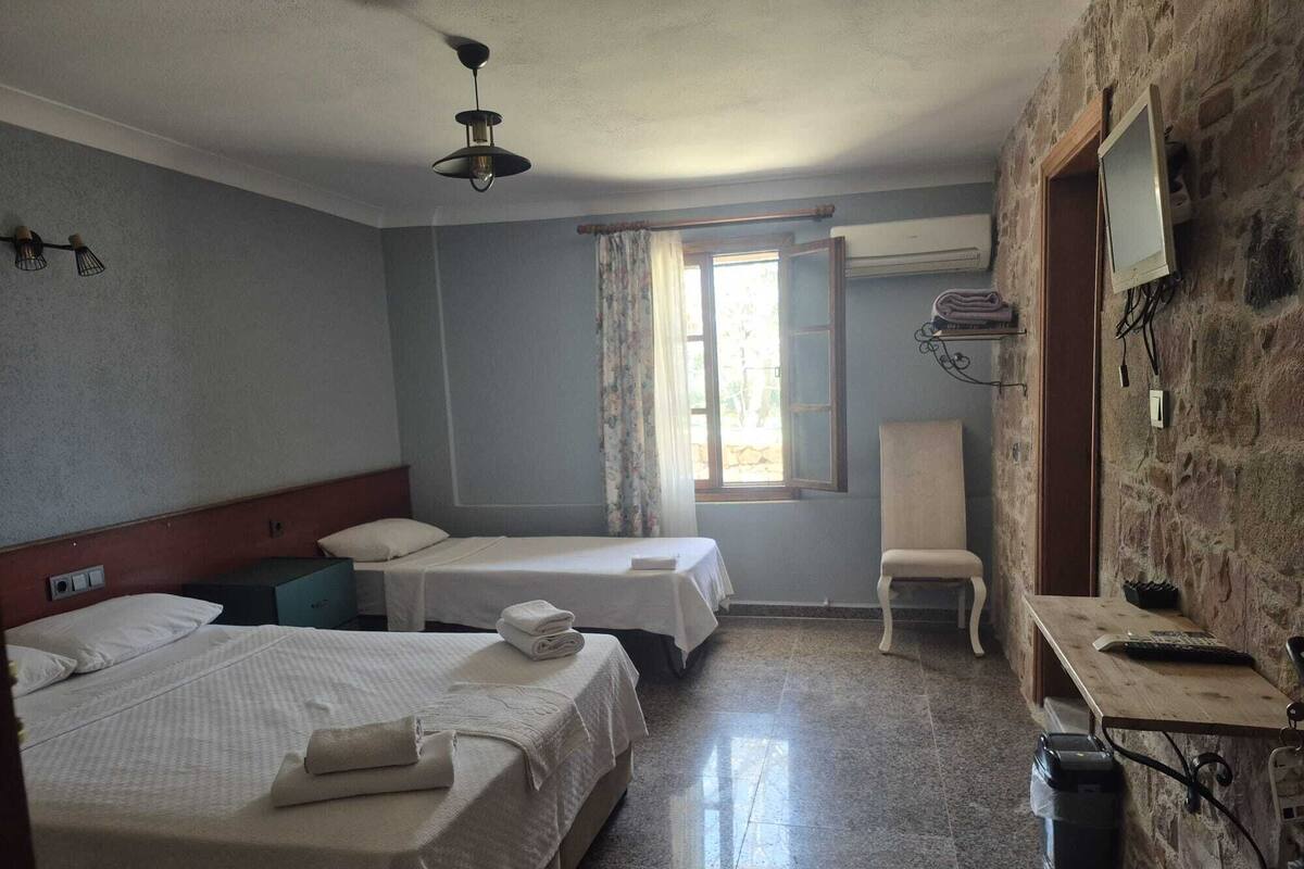 A hotel room with two beds, a chair, a desk with a computer, a TV, and a window with curtains.