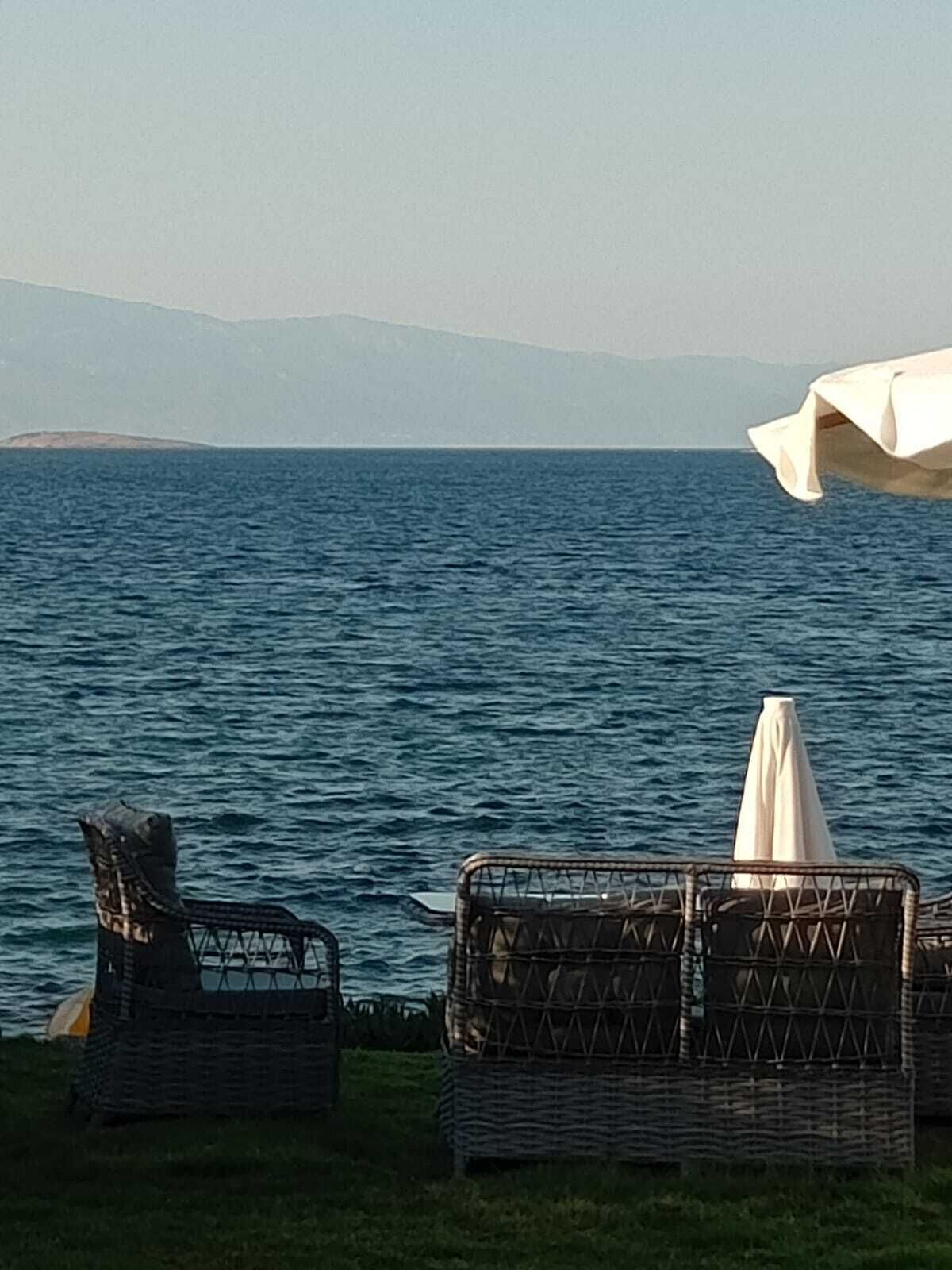 En utsikt över havet med flätade stolar och ett vitt parasoll.