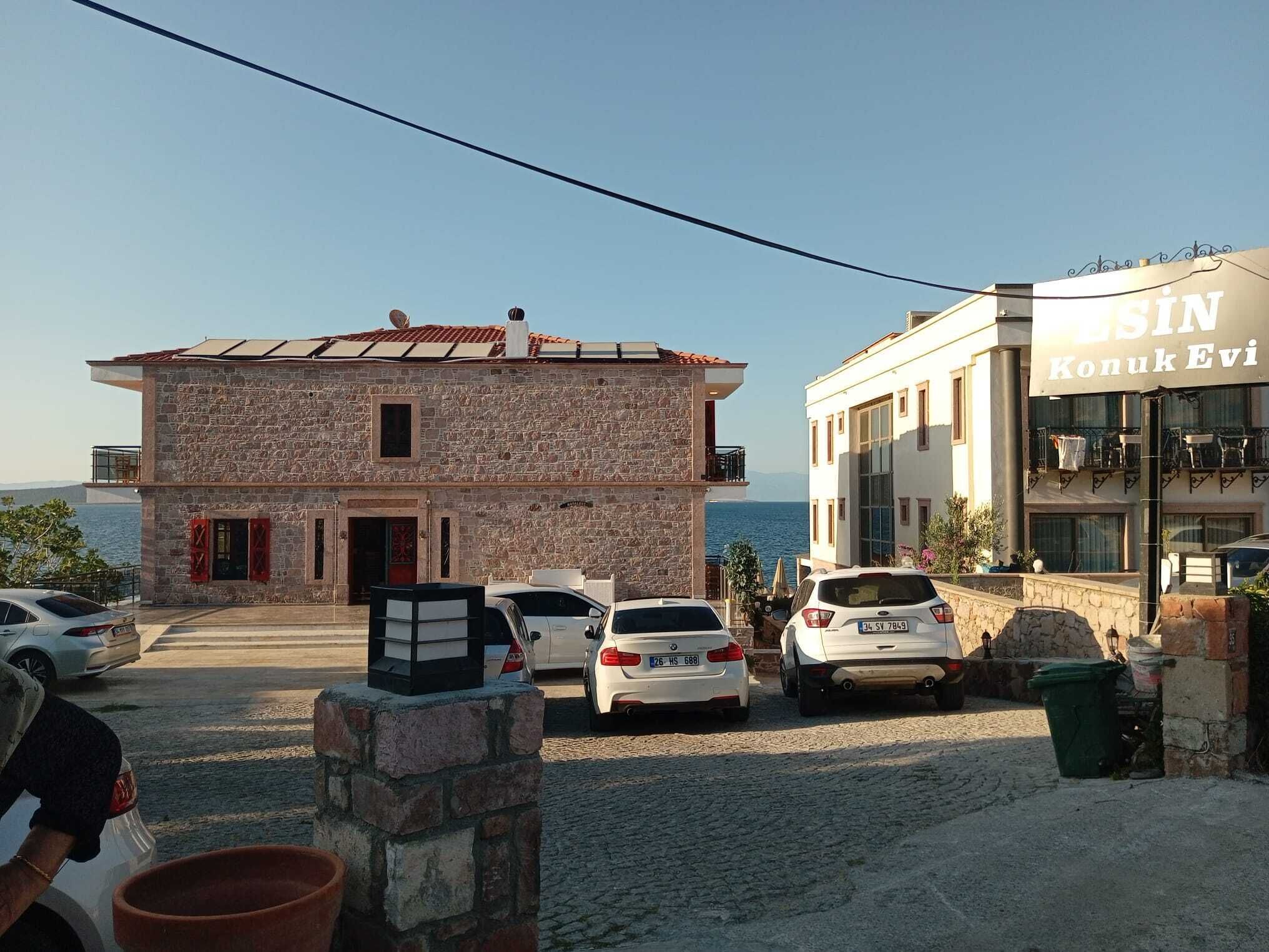 A stone building with a red door and a white building with a sign reading "ESIN Konuk Evi". There are cars parked in front.