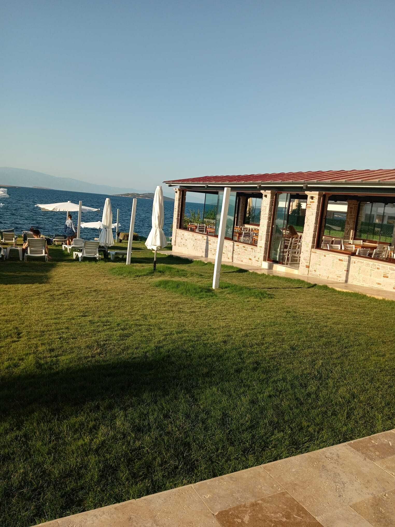 A seaside restaurant with outdoor seating, a stone building, and a view of the sea.