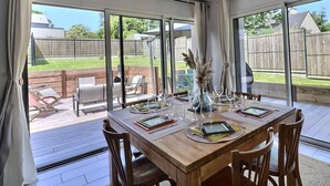 Ein Essbereich mit großem Tisch für sechs Personen, großen Fenstern und Blick auf den Garten.