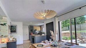 Eine moderne Küche mit einer zentralen Kochinsel, einem Essbereich mit Tisch für sechs Personen und einem großen Fenster mit Blick ins Freie.