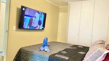 Un dormitorio con una cama cubierta por un colcha, un televisor en la pared y un armario.