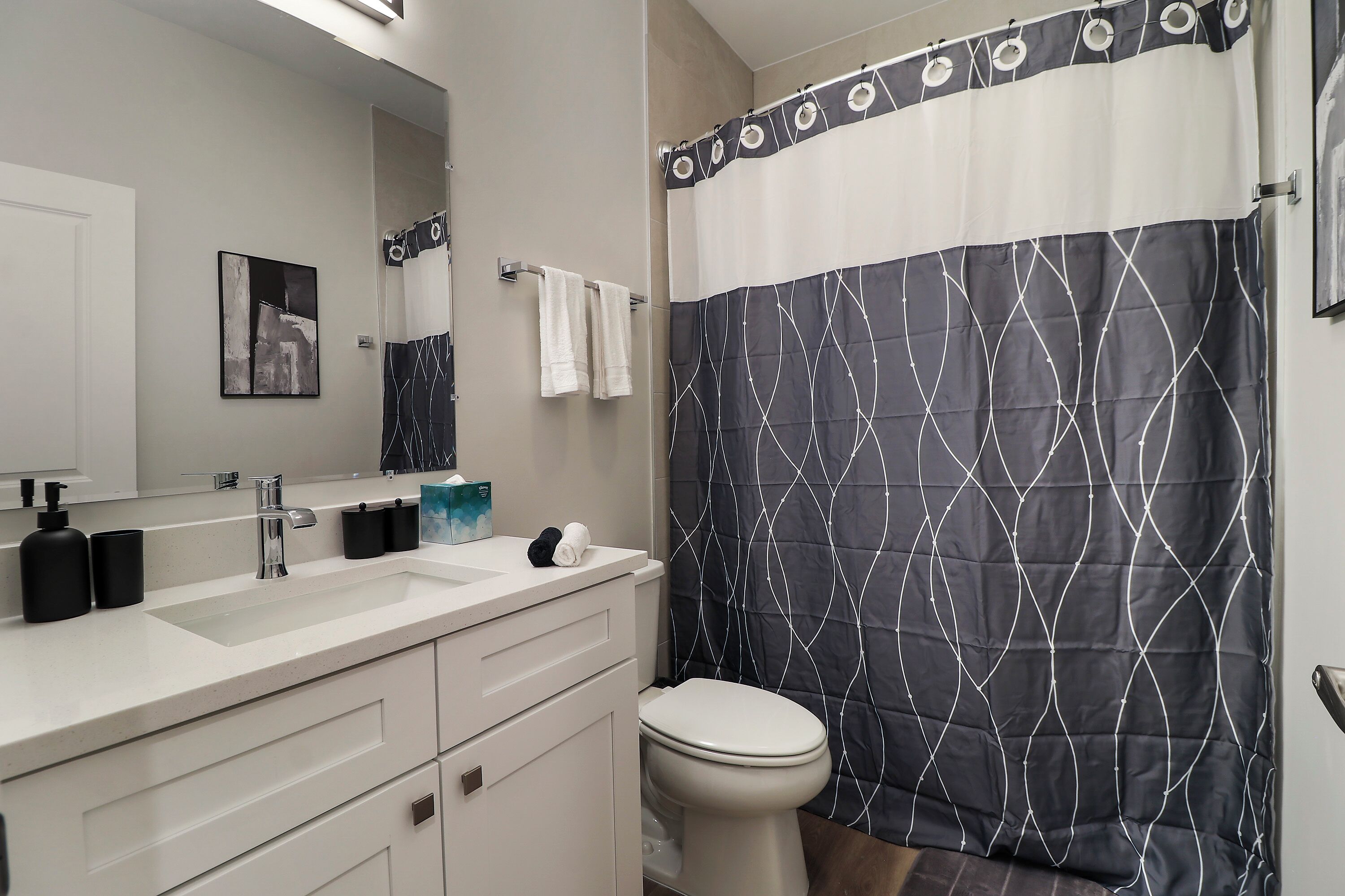 A bathroom with a white sink, a mirror, a toilet, and a shower curtain with a geometric pattern.