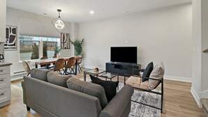 A modern living room with a sofa, TV, dining area, and large windows overlooking a body of water. - Warrenville Rep 2 (Warrenville)