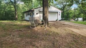 A rustic cabin with a swing chair, surrounded by trees and a dirt path. - 1-bedroom, dog friendly cottage (Hot Springs)