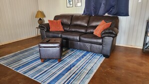 A brown leather sofa with orange cushions, a matching ottoman, and a striped blue and white rug. - 1-bedroom, dog friendly cottage (Hot Springs)