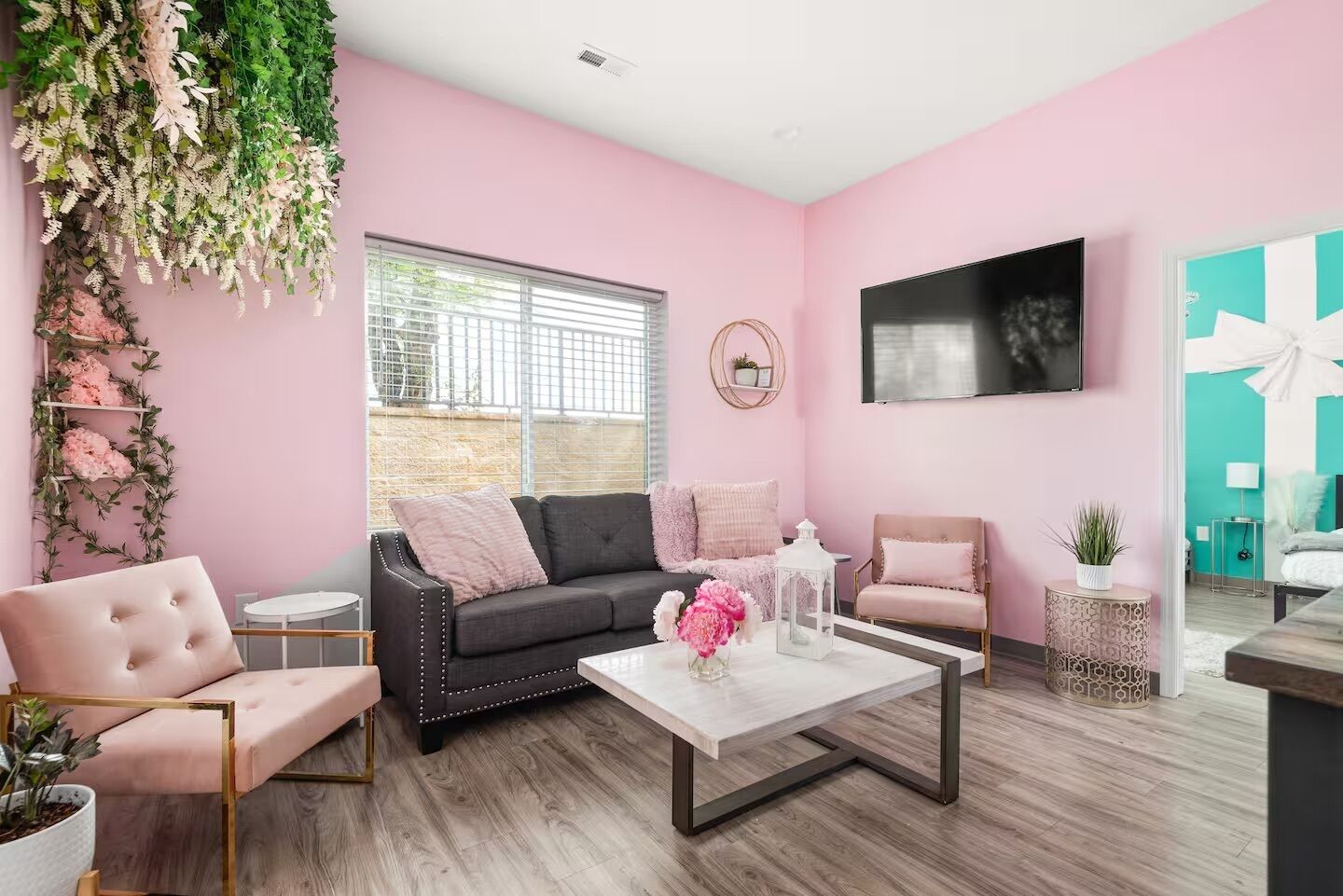 Una habitación con pared rosa, sofá negro, una mesa de centro blanca y sillón rosa.