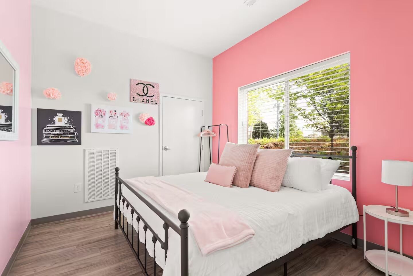 A bedroom with a bed, a window with blinds, a bedside table, and wall decorations.