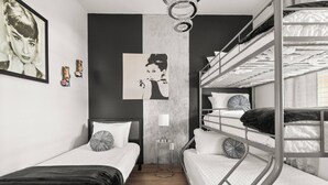 Een kamer met twee eenpersoonsbedden, een stapelbed, een wandlamp en een lijst met een afbeelding.