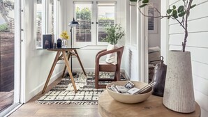 A cozy reading nook with a wooden chair, a small table with a bowl and books, a lamp, and a potted plant.