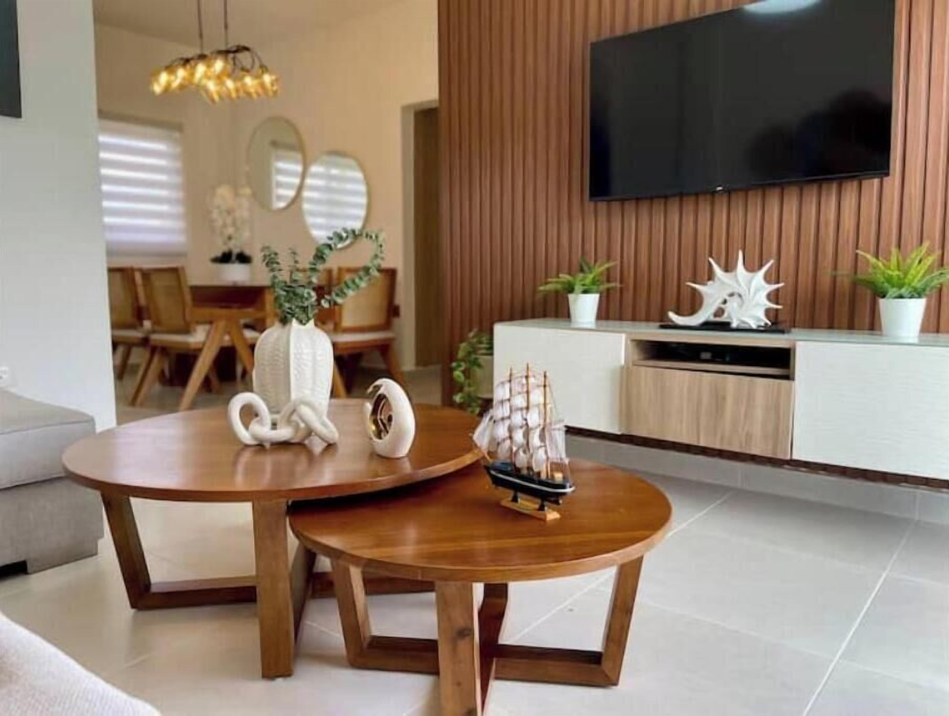 A modern living room with a wooden coffee table, a small ship model, and a flat-screen TV mounted on a wooden wall.