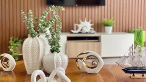 A wooden dining table with white decorative items, a TV mounted on a wooden wall, and a small ship model.