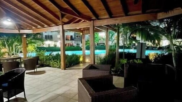 An outdoor patio area with wooden beams, tiled flooring, and wicker furniture.